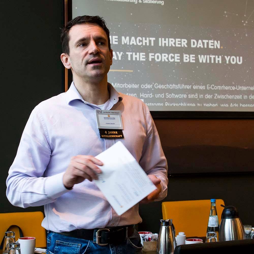 Frank Geiger hält einen Vortrag vor einem Unternehmer-Netzwerk, mit Namensschild und Präsentationsfolie im Hintergrund